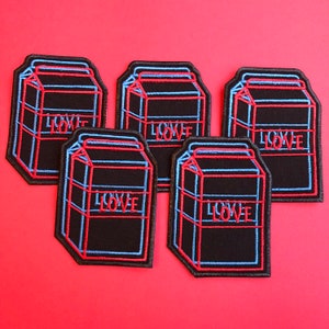 Peut inclure: Cinq patchs thermocollants brodés noirs et bleus en forme de briques de lait avec le mot "LOVE" en lettres rouges.