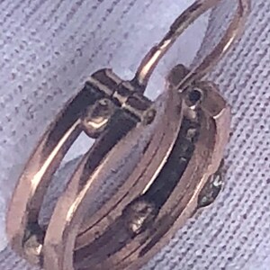K&ouml;nnte beinhalten: Nahaufnahme eines goldfarbenen Creolen-Ohrrings mit Klappverschluss. Der Ohrring hat ein mehrschichtiges Design mit einem kleinen, m&ouml;glicherweise Edelstein-Akzent. Das Metall hat ein warmes, antikes Aussehen.