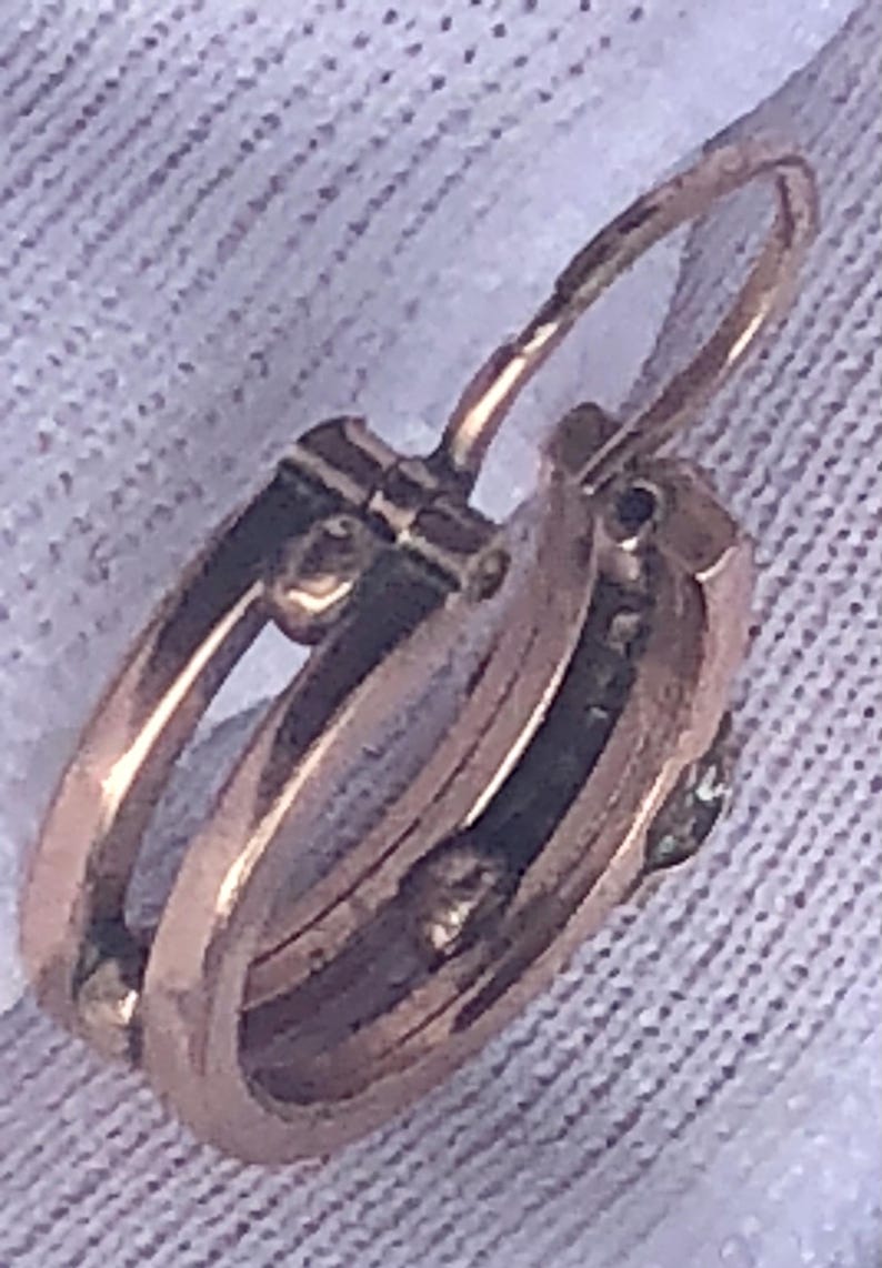 K&ouml;nnte beinhalten: Nahaufnahme eines goldfarbenen Creolen-Ohrrings mit Klappverschluss. Der Ohrring hat ein mehrschichtiges Design mit einem kleinen, m&ouml;glicherweise Edelstein-Akzent. Das Metall hat ein warmes, antikes Aussehen.