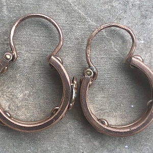 K&ouml;nnte beinhalten: Ein Paar antike Creolen aus Ros&eacute;gold. Jeder Ohrring hat einen Klappverschluss und kleine dekorative Elemente. Die Ohrringe werden vor einem strukturierten, grauen Hintergrund pr&auml;sentiert, der ihren Vintage-Charme und ihr Design hervorhebt.