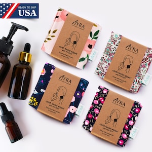 Puede incluir: Un surtido de toallitas faciales de tela con estampados florales, empaquetadas con bandas de papel marrón. Las toallitas están etiquetadas como "AYRA" e incluyen el texto "cloth facial wipes with POCKET. Super soft and gentle on your skin." También se ven varias botellas de vidrio ámbar.