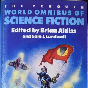 May include: A vintage paperback book titled "The Penguin World Omnibus of Science Fiction". The cover art depicts a science fiction scene with a figure holding a flag, spaceships, and a futuristic cityscape. Edited by Brian Aldiss and Sam J. Lundwall.