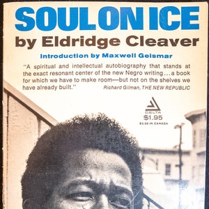 May include: Book cover for "Soul on Ice" by Eldridge Cleaver. The title is in blue, with the author's name below. The cover features a black and white portrait of a man. Text includes a quote and the publisher's logo.