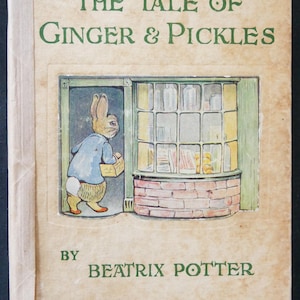 May include: Vintage hardcover book titled "The Tale of Ginger & Pickles" by Beatrix Potter. The cover features a color illustration of a rabbit in a blue coat, carrying a basket, standing outside a shop window. The book's title and author's name are in green.