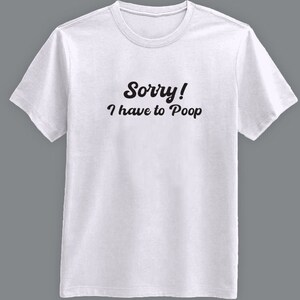 May include: White t-shirt with the text "Sorry! I have to Poop" in black, casual font. The shirt has a crew neck and short sleeves. The background is a solid gray.