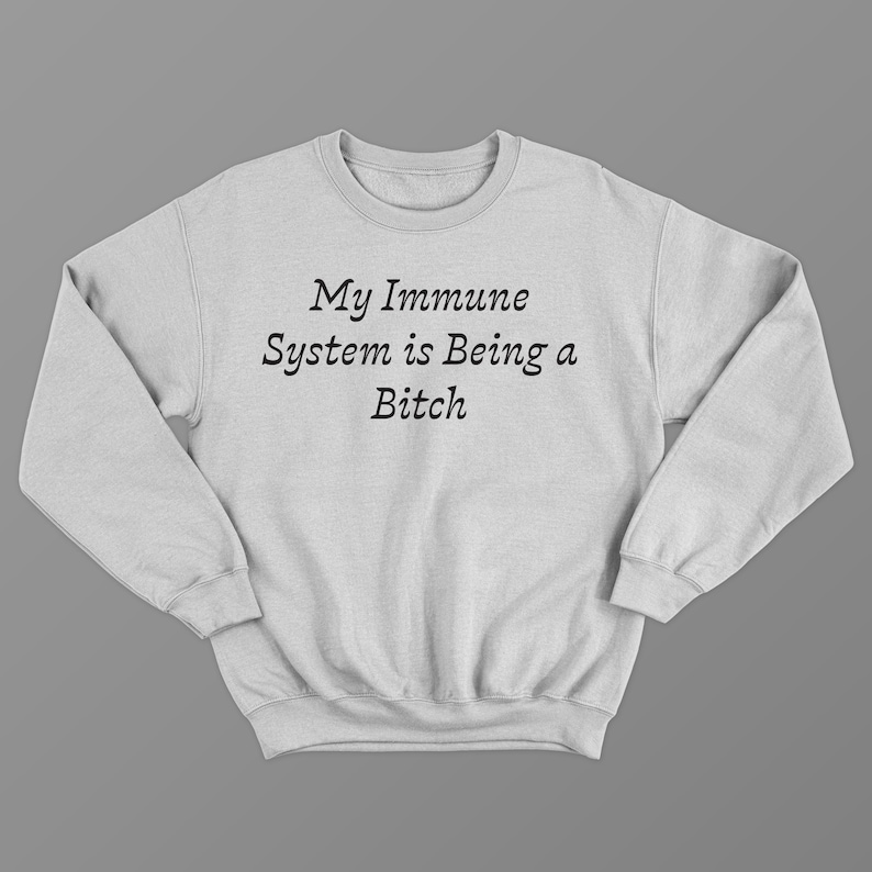 May include: Light gray sweatshirt with the text "My Immune System is Being a Bitch" in black. The sweatshirt has a crew neck and long sleeves. The background is a solid gray.