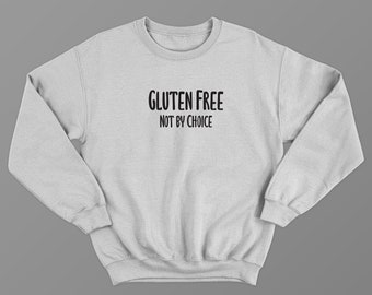 May include: A light gray sweatshirt with the text "GLUTEN FREE NOT BY CHOICE" in black, centered on the front. The sweatshirt has a crew neck and long sleeves, suitable for casual wear.