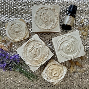 Può includere: Quattro saponette quadrate color bianco sporco con un motivo a spirale color crema sulla parte superiore, una piccola boccetta di vetro marrone scuro con etichetta, un mazzetto di lavanda secca viola e frammenti di resina marrone chiaro.