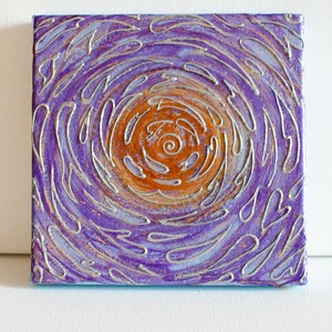 May include: Abstract painting on canvas with a swirling purple and silver design. The centre of the painting features a circular orange and gold design.