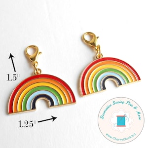 May include: Two rainbow charms with gold-colored clasps. Each charm is a half-circle with red, orange, yellow, green, blue, and black stripes. The charms are 1.5 inches tall and 1.25 inches wide.
