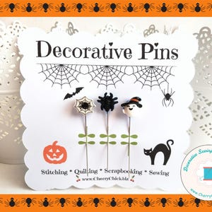 May include: Decorative pins with Halloween-themed designs. The pins feature a spider web, a bat, a spider, a black spider, and a ghost wearing a witch hat. The card also includes a pumpkin, a black cat, and text that reads "Decorative Pins".