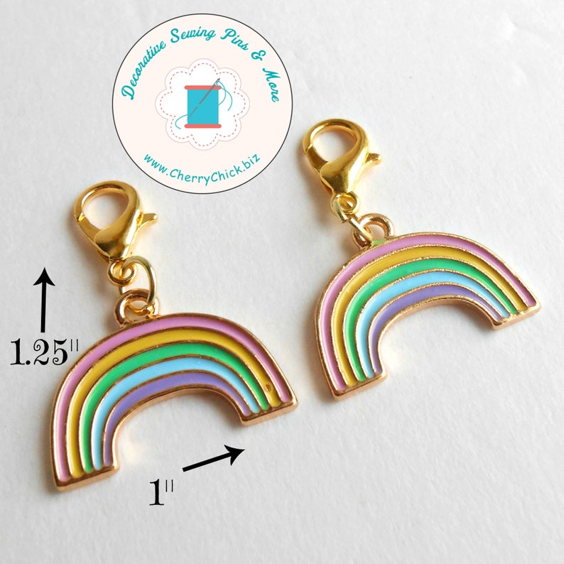 May include: Two gold-colored rainbow charms, each 1.25 inches tall and 1 inch wide, with a lobster clasp. The rainbow design features pastel colors: yellow, green, blue, and purple. The charms are for decorative sewing pins and more.