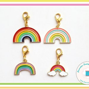 May include: Four colorful rainbow charms with gold-colored clasps. Each charm features a different rainbow design with various colors, including red, orange, yellow, green, blue, and purple. The charms are likely for jewelry or craft projects.