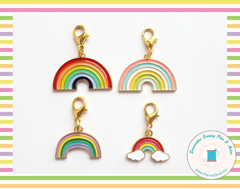 May include: Four colorful rainbow charms with gold-colored clasps. Each charm features a different rainbow design with various colors, including red, orange, yellow, green, blue, and purple. The charms are likely for jewelry or craft projects.