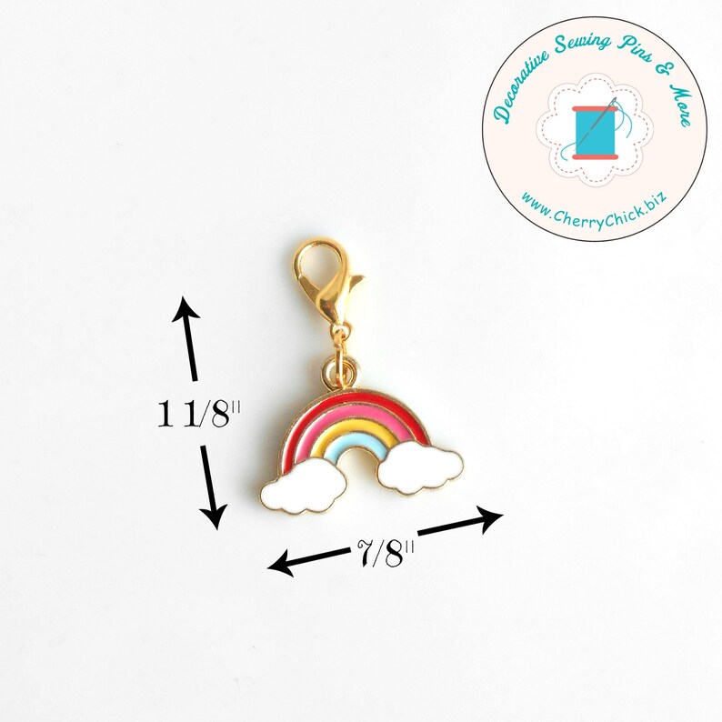 May include: A gold-colored charm with a rainbow design, featuring red, pink, yellow, and blue arches, and white cloud accents. The charm is 1 1/8 inches tall and 7/8 inches wide. It has a lobster clasp for easy attachment. The charm is from Decorative Sewing Pins & More.