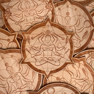 May include: A set of wooden coasters featuring intricate laser-cut designs of a person in a meditative pose surrounded by geometric patterns. The coasters are made of light brown wood and have a natural finish.