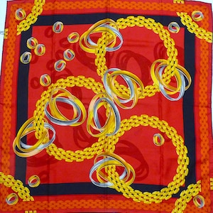 May include: A red silk scarf with a black border and a pattern of gold and silver interlocking rings and chains.