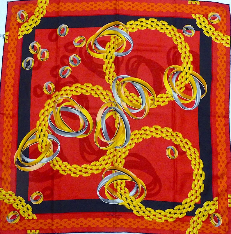 May include: A red silk scarf with a black border and a pattern of gold and silver interlocking rings and chains.