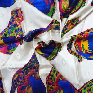 May include: A white silk scarf with a repeating pattern of colorful leopards. The leopards are made up of bright colors including red, yellow, blue, green, and pink. The scarf has a subtle embossed pattern of the word 'Cartier' repeated throughout.