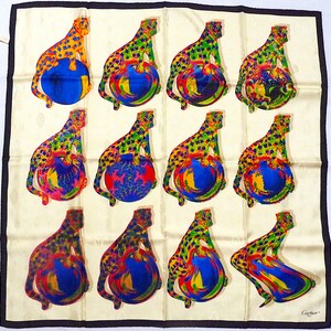 May include: A white silk scarf with a black border. The scarf features a repeating pattern of 12 leopards sitting on top of colorful globes. The leopards are yellow, green, and red with black spots. The globes are blue, red, and yellow with white and black swirls. The scarf is signed 'Cartier' in the lower right corner.