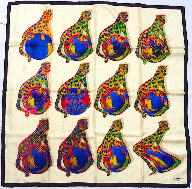 May include: A white silk scarf with a black border. The scarf features a repeating pattern of 12 leopards sitting on top of colorful globes. The leopards are yellow, green, and red with black spots. The globes are blue, red, and yellow with white and black swirls. The scarf is signed 'Cartier' in the lower right corner.