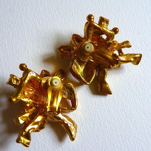 K&ouml;nnte beinhalten: Ein Paar goldfarbene Ohrclips mit floralem Design. Die Ohrringe sind aus Metall und haben eine strukturierte Oberfl&auml;che.