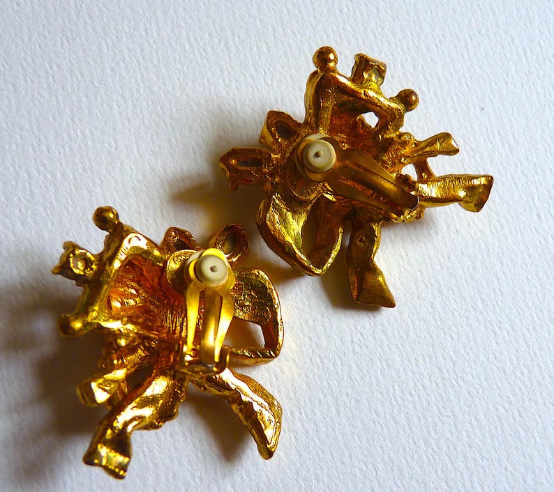 K&ouml;nnte beinhalten: Ein Paar goldfarbene Ohrclips mit floralem Design. Die Ohrringe sind aus Metall und haben eine strukturierte Oberfl&auml;che.