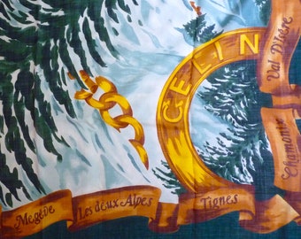 Op de afbeelding: Een groene en witte stof met een gouden cirkel en de tekst "CELIN" erin. De cirkel wordt omringd door een bruin lint met de tekst "Val D'Isere" en "Chamonix" erop. Er zijn ook kleinere linten met de tekst "Megève", "Les deux Alpes" en "Tignes".