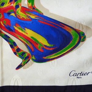 May include: A white silk scarf with a colorful abstract design of a shoe. The scarf has a black border and the words 'Cartier® Paris' printed in the bottom right corner.