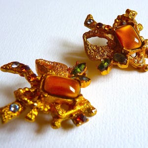 K&ouml;nnte beinhalten: Ein Paar goldfarbene Ohrringe mit strukturiertem Design und orangefarbenen, gr&uuml;nen und violetten Edelsteinen.