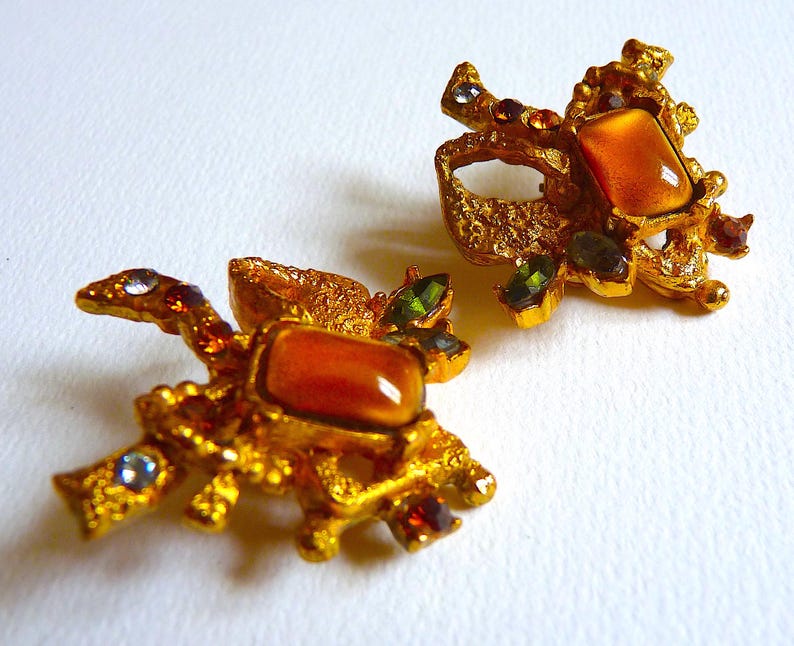 K&ouml;nnte beinhalten: Ein Paar goldfarbene Ohrringe mit strukturiertem Design und orangefarbenen, gr&uuml;nen und violetten Edelsteinen.