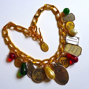 Puede incluir: Un collar de cadena dorada con m&uacute;ltiples dijes, incluyendo cuentas de vidrio rojas y verdes, dijes dorados con el texto "JF Paris" y "Jacques Fath Paris", y un dije plateado con el texto "Avenue des Champs-&Eacute;lys&eacute;es".