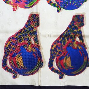 May include: A white silk scarf with a black border. The scarf features a repeating pattern of a stylized leopard with a blue sphere. The leopard is depicted in shades of red, yellow, green, and blue.