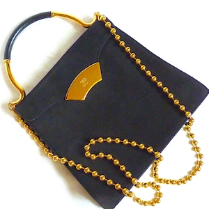 Op de afbeelding: Een zwarte suède handtas met een gouden kettingband en een gouden bovenhandvat. De tas heeft een gouden logo aan de voorkant.