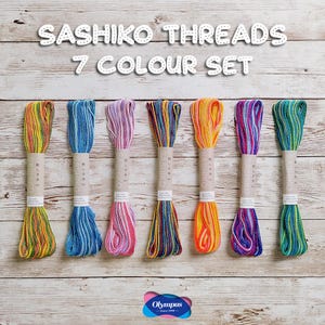 May include: A collection of seven skeins of Sashiko threads in a variety of colours, including blue, pink, yellow, and green. Each skein is wrapped in paper. The text "Sashiko Threads 7 Colour Set" is at the top of the image.