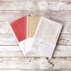 May include: Three quilted kitchen cloths in red, beige, and white with a chevron pattern. The cloths are packaged in plastic and labeled "COSMO", "LECien", and "COSMO 綿麻 マルチクロス".