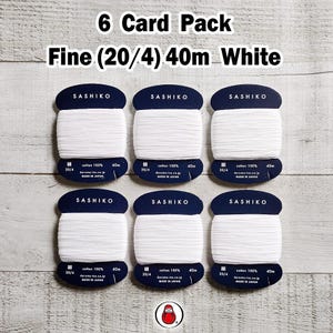 May include: A pack of six white Sashiko thread cards. Each card has a dark blue label with the brand name and thread details. The text on the cards reads "6 Card Pack Fine (20/4) 40m White". The thread is cotton.
