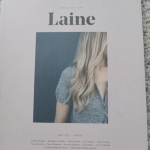 Puede incluir: Una portada de revista gris claro con el título "Laine" en letras grandes y en negrita. La portada presenta una foto de una persona con un top de punto gris. También es visible el texto "NOR FIVE - PASTEL".