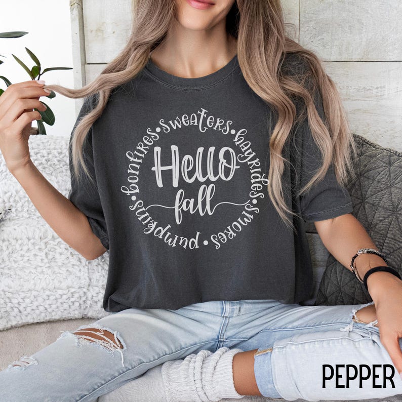May include: A dark gray t-shirt with a white circle graphic that says "Hello Fall" surrounded by the words "bonfires, sweaters, hayrides, smokes, pumpkins".