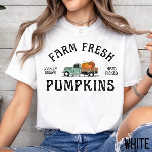 Peut inclure: T-shirt blanc avec un graphique d'un camion vintage transportant des citrouilles. Le texte "Farm Fresh Locally Grown Hand Picked Pumpkins" est imprimé sur le t-shirt.