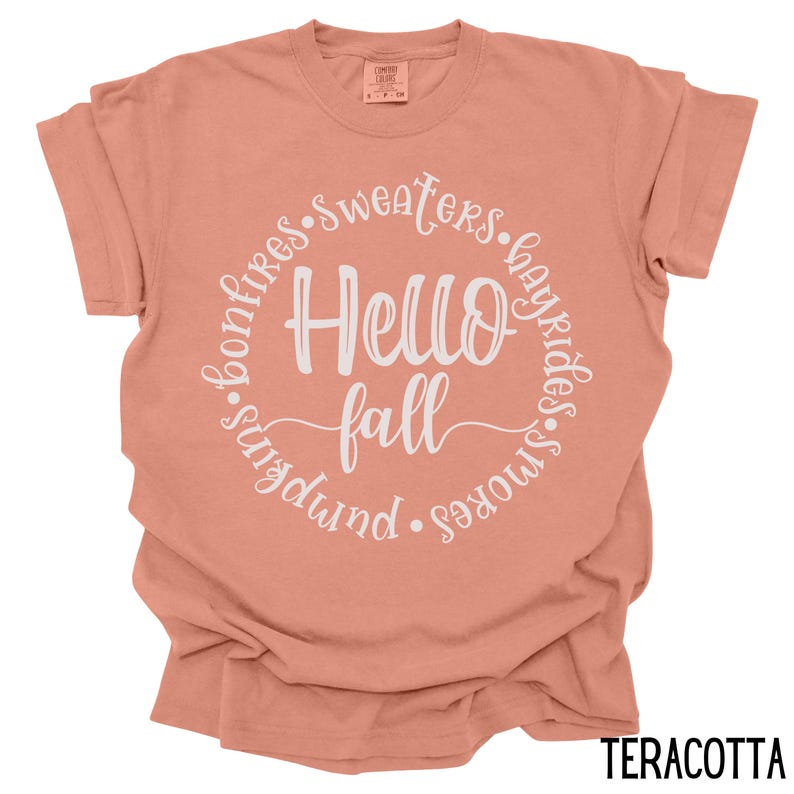 May include: Terracotta t-shirt with a white circle graphic that says "Hello Fall" surrounded by the words "bonfires, sweaters, hayrides, s'mores, pumpkin".