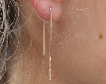May include: A pair of silver dangle earrings with a simple, straight design. The earrings are long and thin, and they hang from the earlobes.