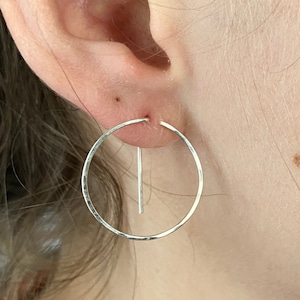 May include: Silver hoop earrings with a straight bar hanging from the bottom of the hoop.