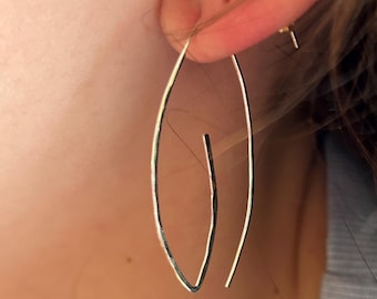 Può includere: Un paio di orecchini a cerchio d'argento con un design unico, leggermente asimmetrico. Gli orecchini sono sottili e delicati e pendono dal lobo dell'orecchio.