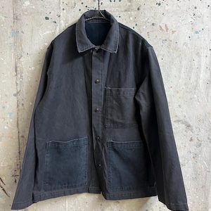 May include: A dark gray work jacket with a collared neckline and button-up front. The jacket has two chest pockets and two lower pockets. It is hanging on a metal hanger against a mottled background.