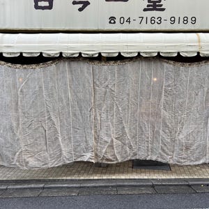 May include: A white awning with a phone number, 04-7163-9189, printed on it. The awning is over a storefront with a white mesh curtain covering the windows.