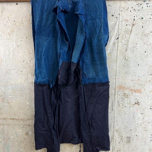 Peut inclure: Un long vêtement sans manches présentant un design bicolore avec une partie supérieure bleu vif et une partie inférieure bleu marine foncé. La pièce est composée de plusieurs panneaux de tissu avec des coutures visibles et un devant ouvert.