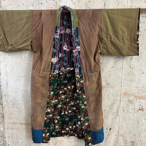 May include: A brown, green, and blue patchwork kimono with floral patterns. The kimono is hanging on a wall.