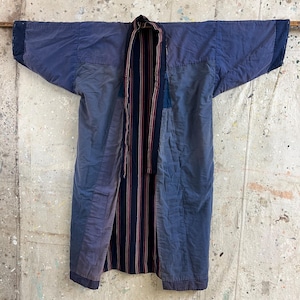 May include: A long, blue quilted robe with a striped sash. The robe is made of patchwork fabric and has a relaxed fit.