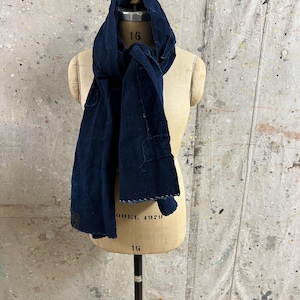 Puede incluir: Una bufanda de color azul marino oscuro drapeada sobre un torso de maniquí beige. La bufanda presenta costuras visibles a lo largo de los bordes, una forma rectangular y una apariencia de tela texturizada. El maniquí muestra el número 16 y el texto MODEL 1979.